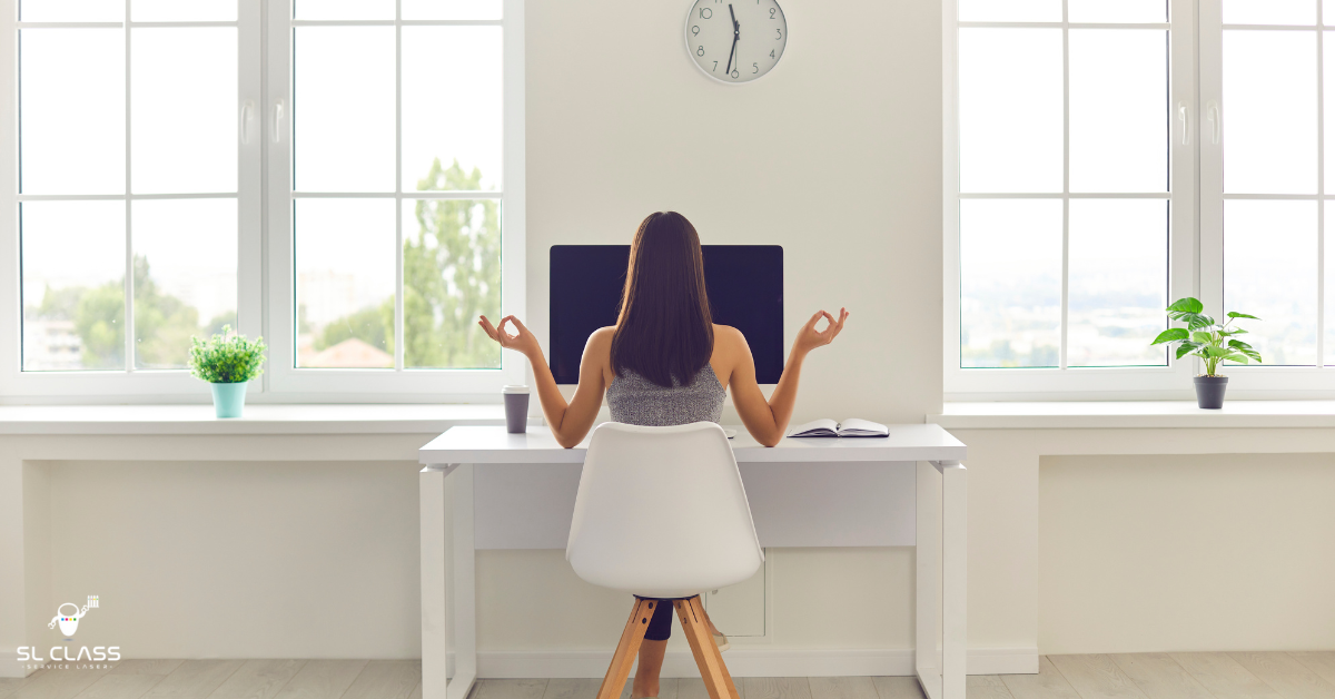 Femme de dos assise à un bureau blanc devant une grande fenêtre, travaillant sur ordinateur dans un espace lumineux et minimaliste.